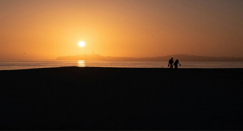 Silhouette of a couple walking hand in hand along the beach at Half Moon Bay against a vivid orange sunset over the Pacific Ocean