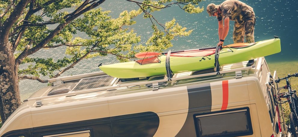 get your RV ready for summer. man secured kayaks to the roof of RV.